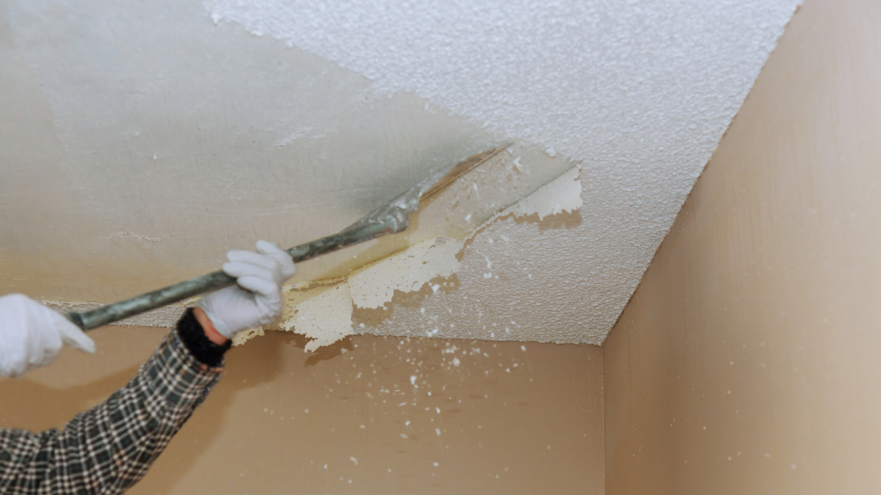 Person scraping textured ceiling with a long-handled tool, creating falling debris.