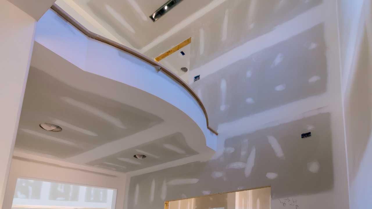 Interior view of a room under construction with drywall on walls and ceiling, arched details, and electrical fixtures.