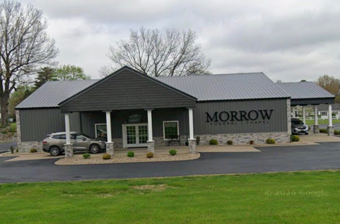 A light-colored, single-story commercial building with a central porch supported by four white columns.