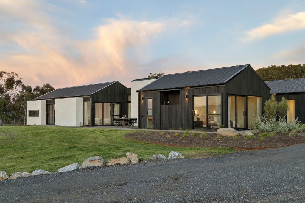 Modern black-and-white cabins on a grassy lot at sunset, with a gravel foreground and trees in back