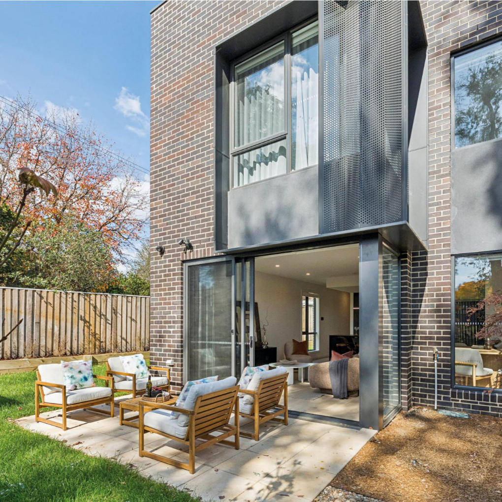 Modern brick townhouse patio with open glass doors, wicker seating, and a small outdoor table under bright daylight