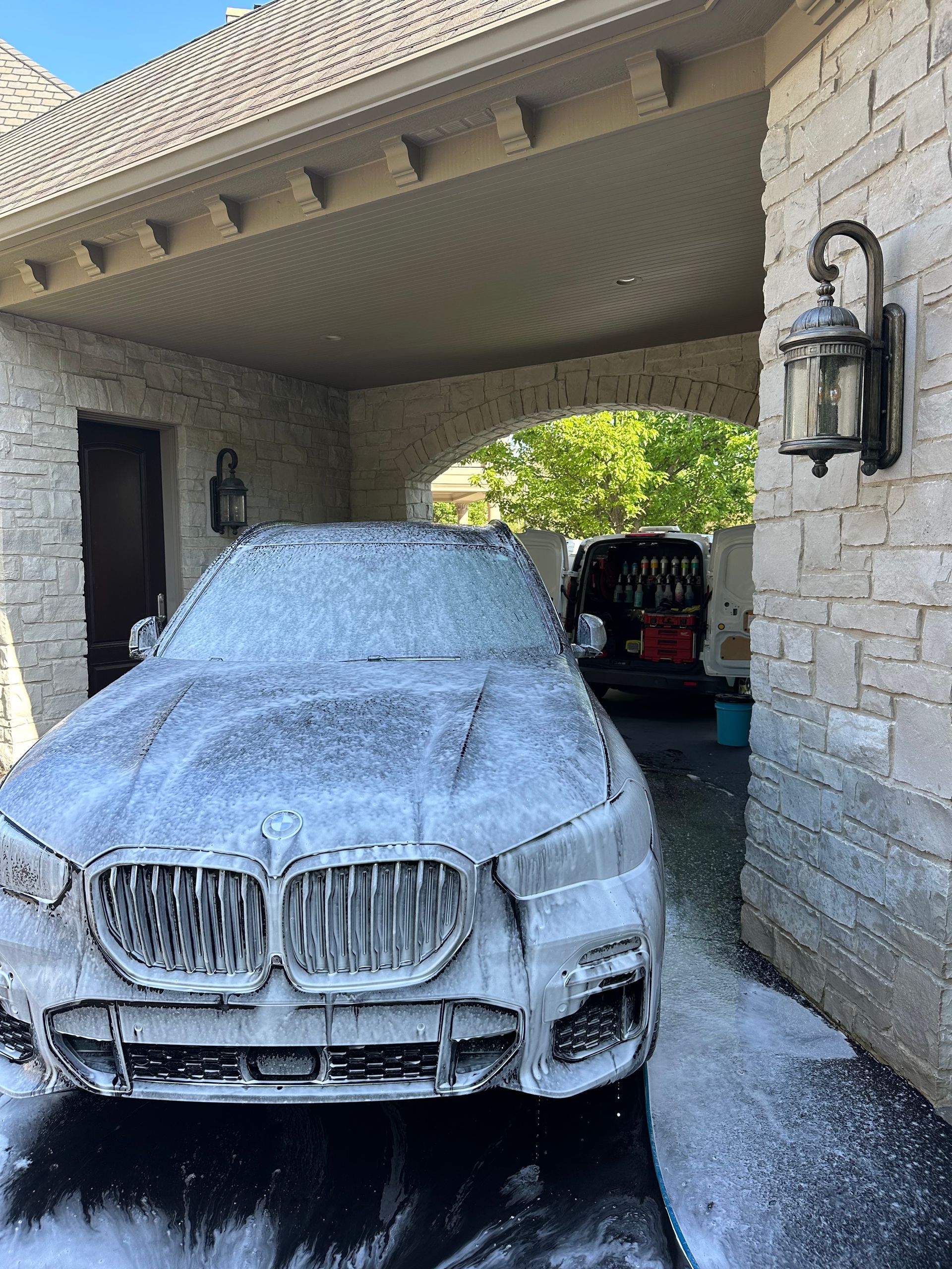 Car covered in foam at a stone driveway car wash under a covered portico