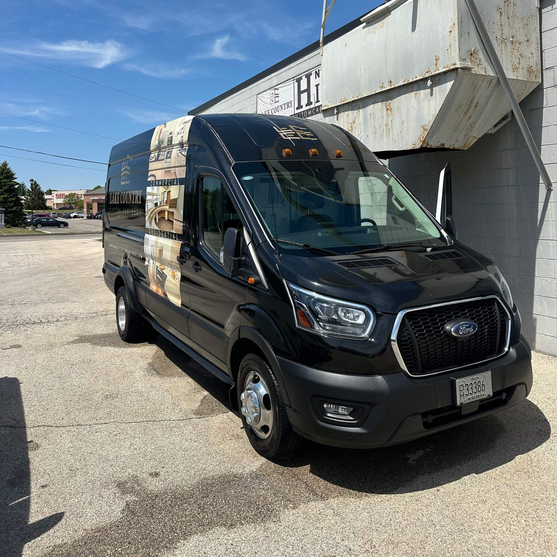 Black commercial van parked beside a white building on a sunny street.
