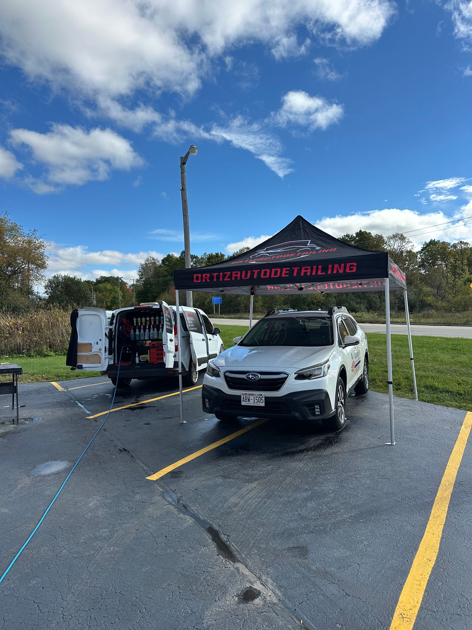 White SUV and van under a black canopy at an outdoor event in a parking lot