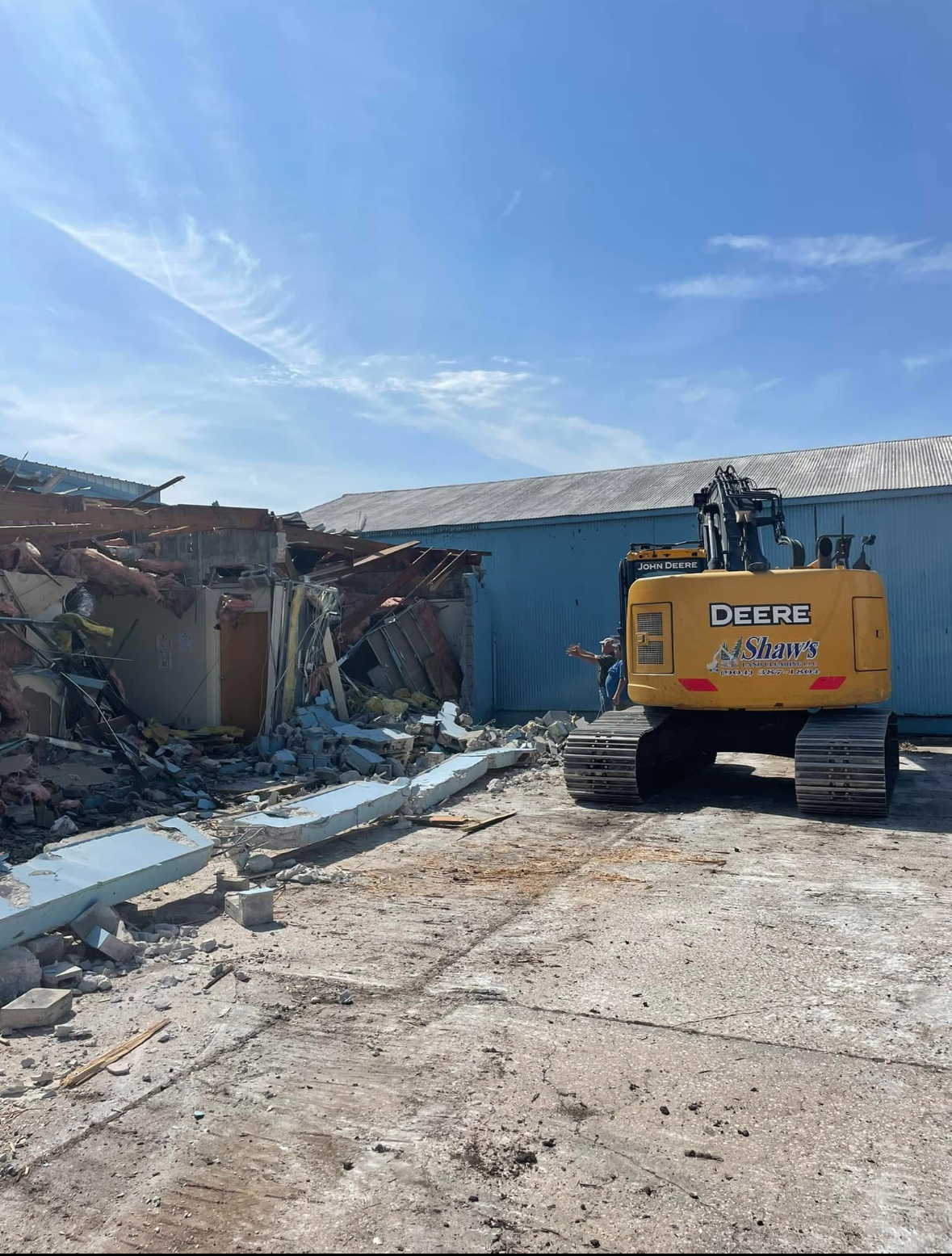A John Deere excavator demolishes a building on a sunny day.
