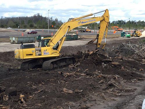 Yellow excavator digging through dirt at a construction site under a cloudy sky