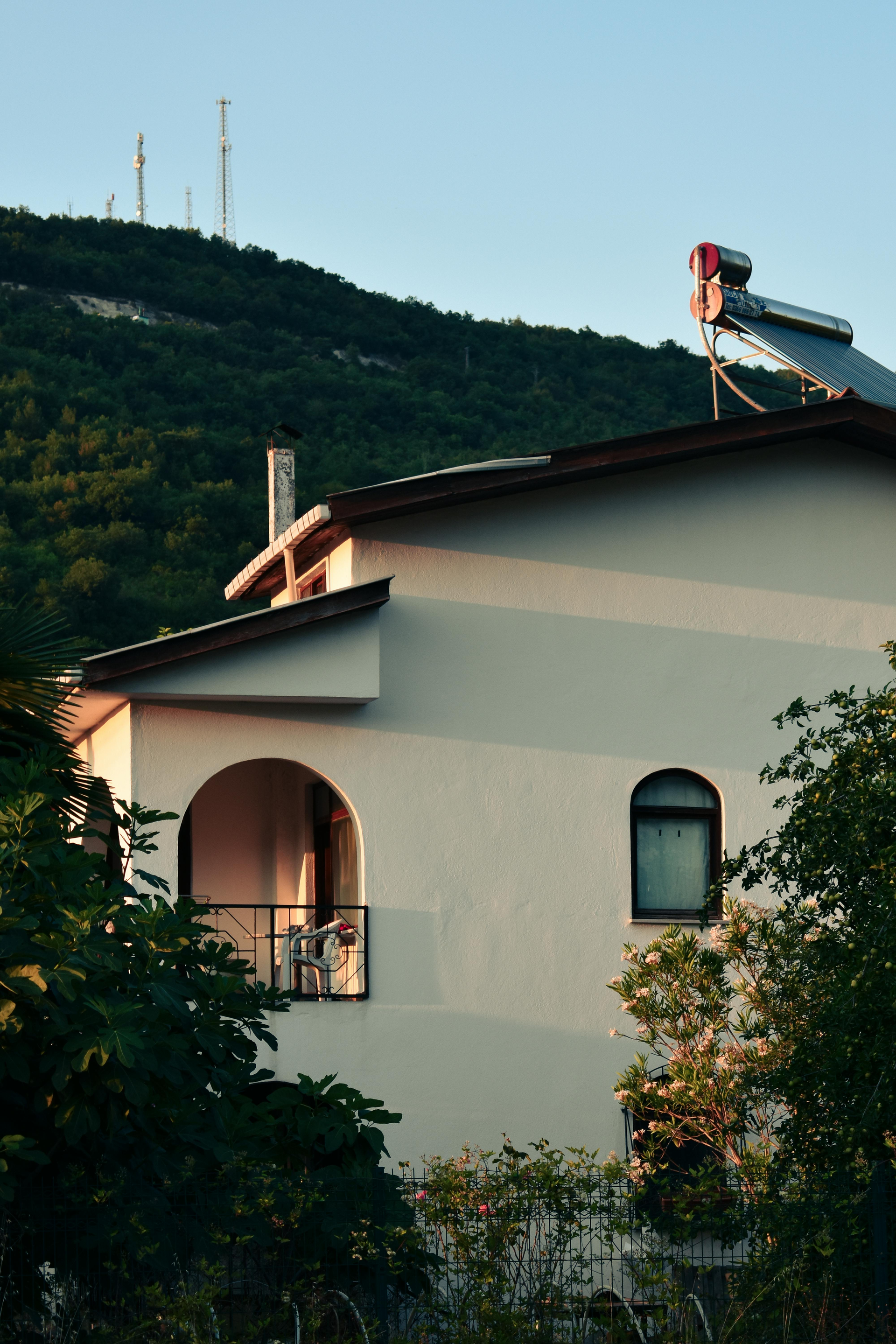 White house with red roof beside a green hillside at dusk