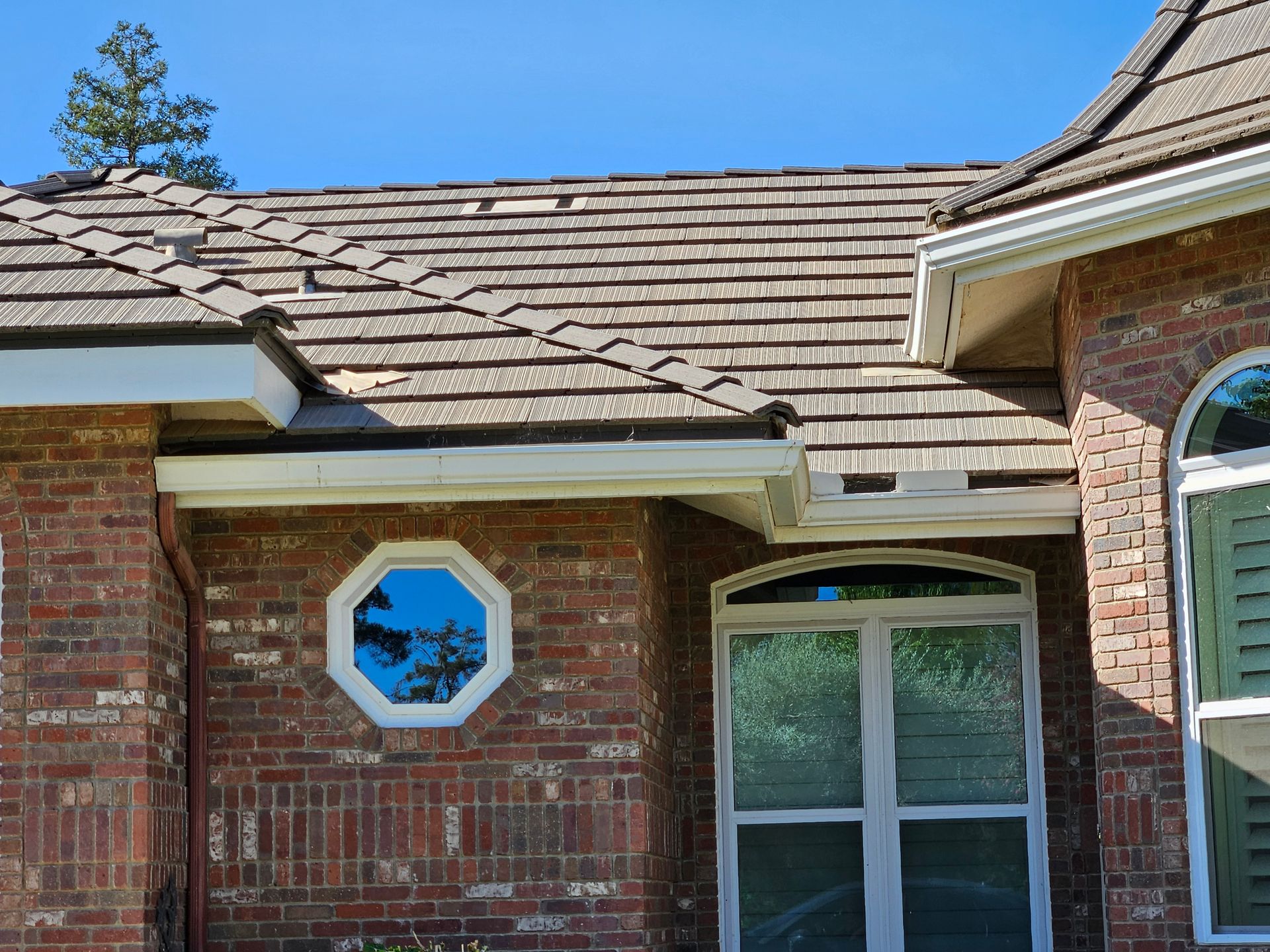 Brick house with octagonal window, wooden shake roof, and white gutters under a blue sky.