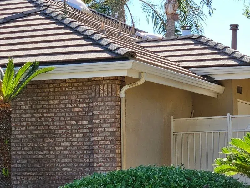 House exterior with brick and stucco walls, brown tile roof, white gutters, and a small green fence.
