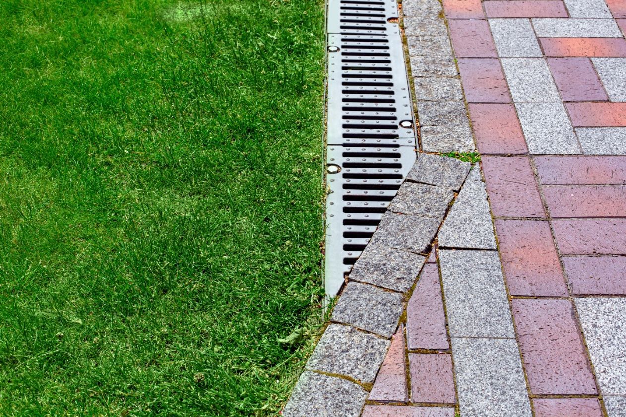 Grassy lawn beside a brick walkway with a metal drainage grate along the edge