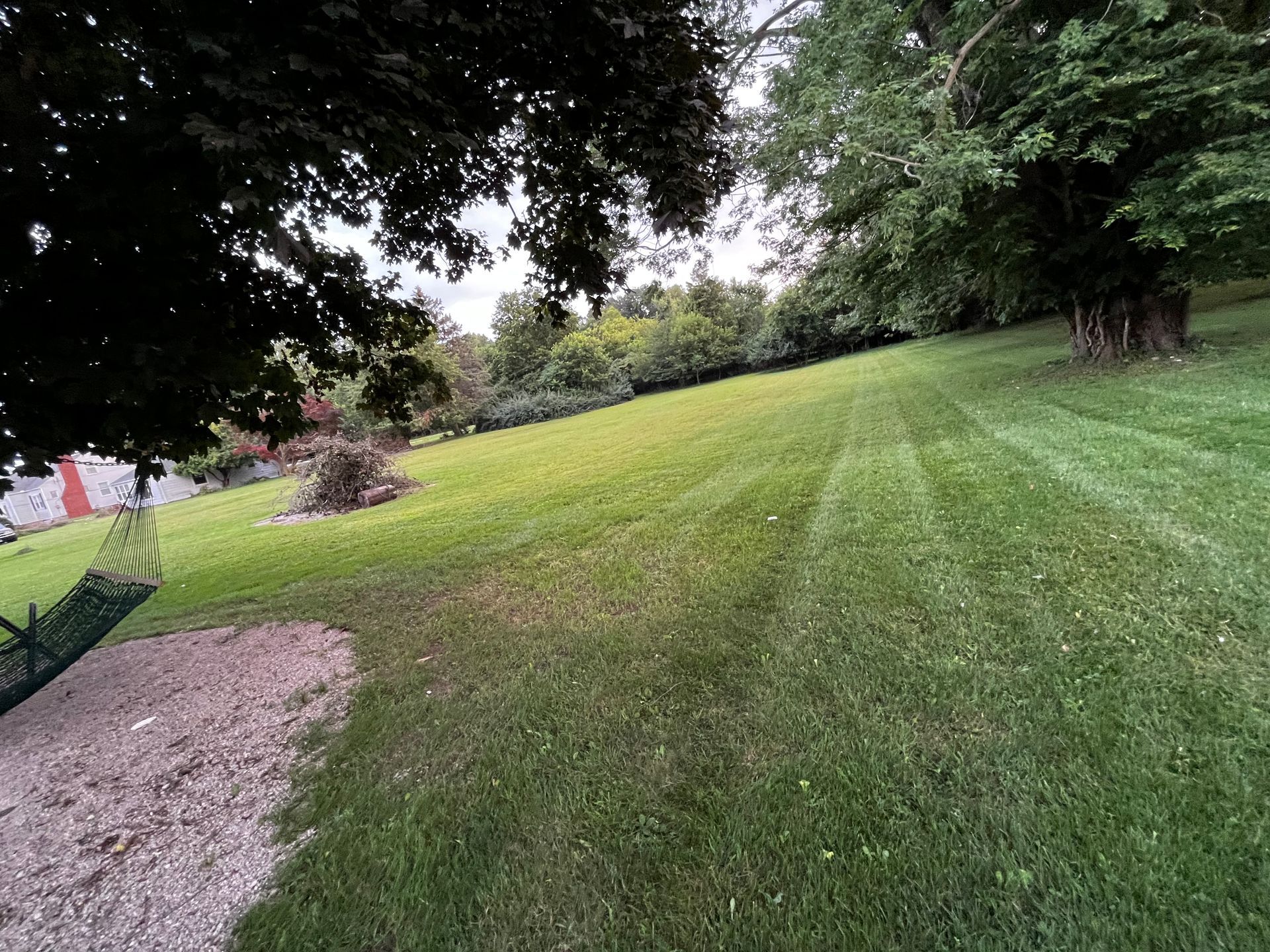 Person operating a red lawn mower on a green lawn beside a stone wall
