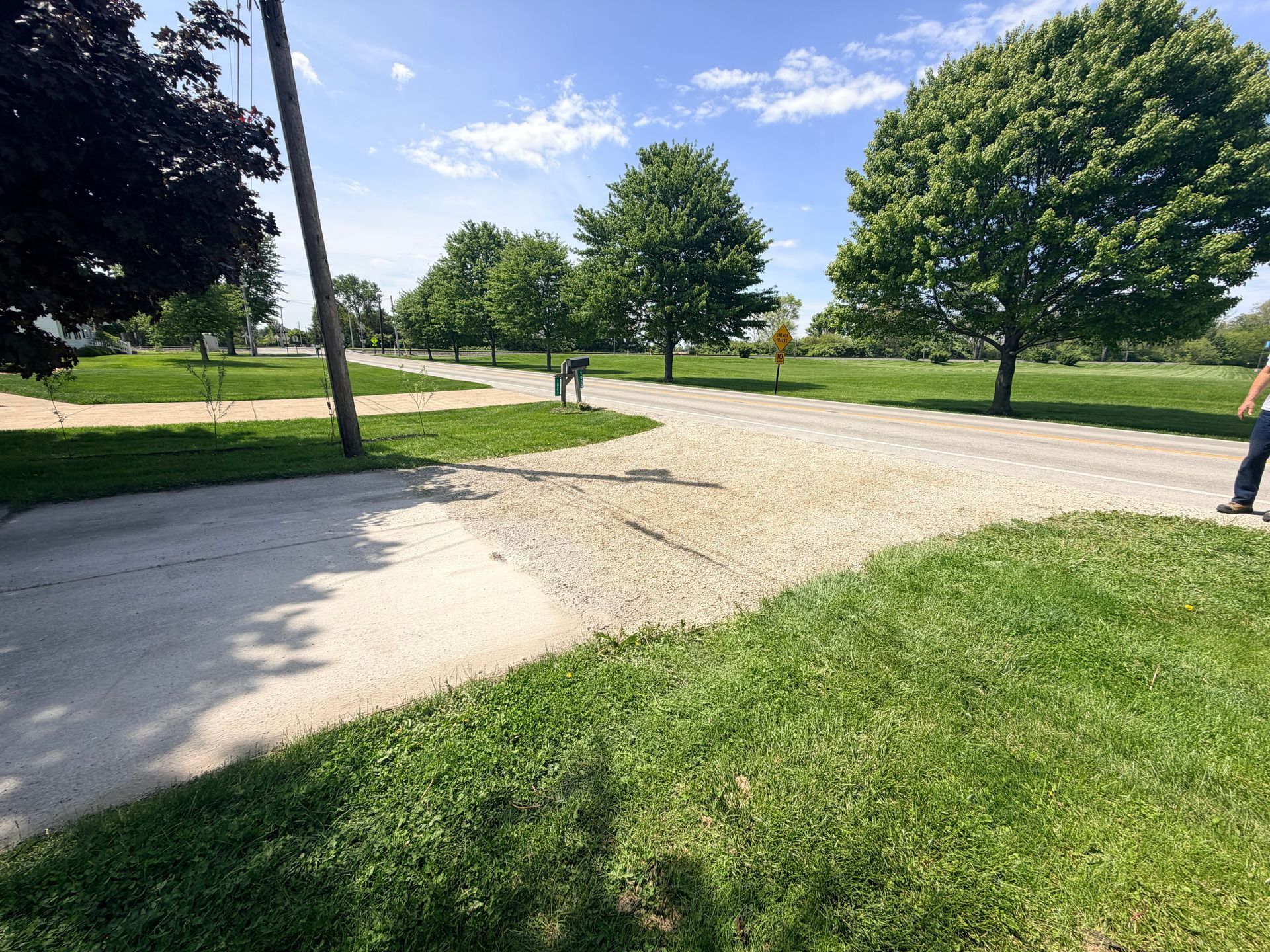 Gravel path curving through a green park with trees and a blue sky