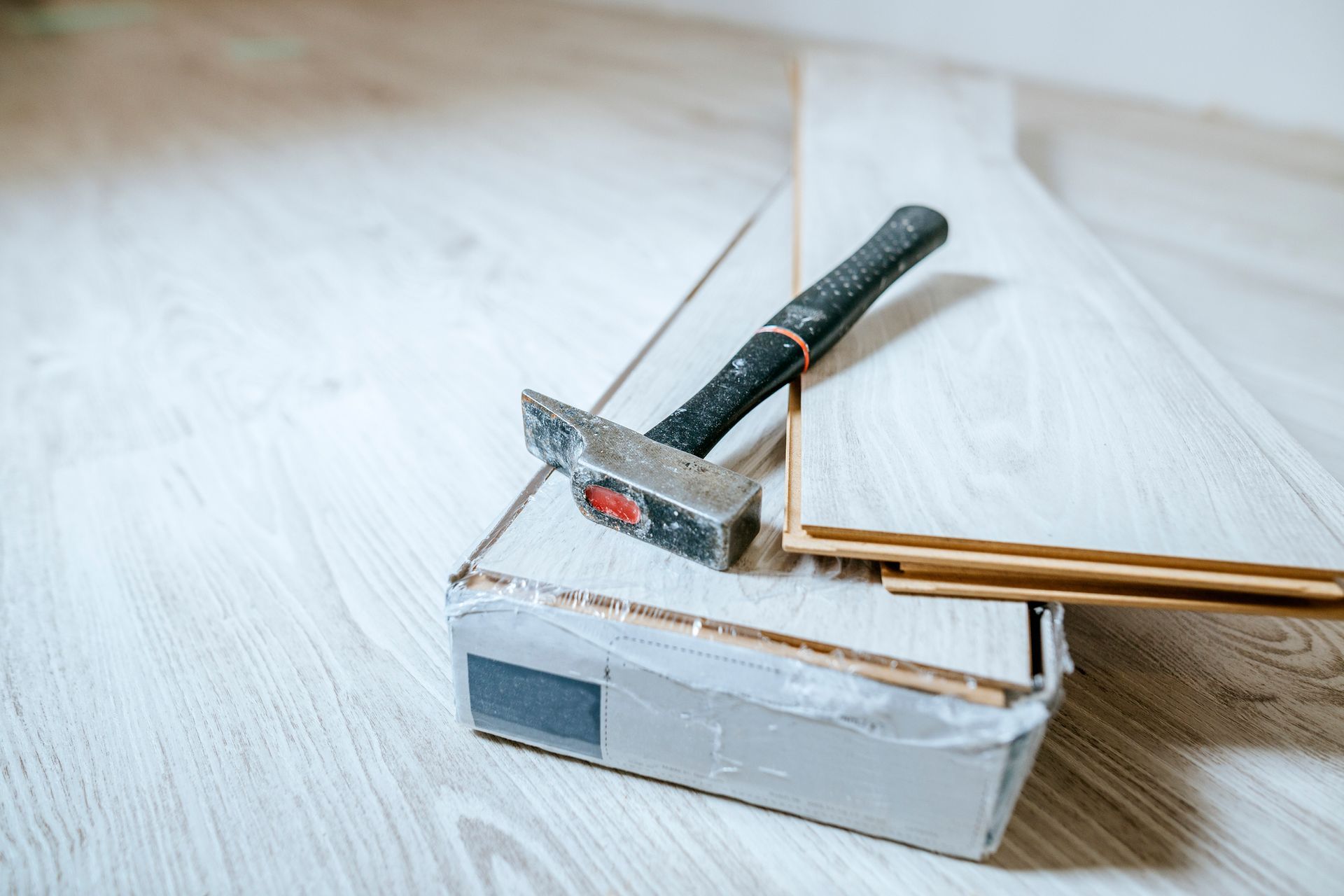 Hammer resting on a cardboard box with wood planks and flooring; a construction site setup.