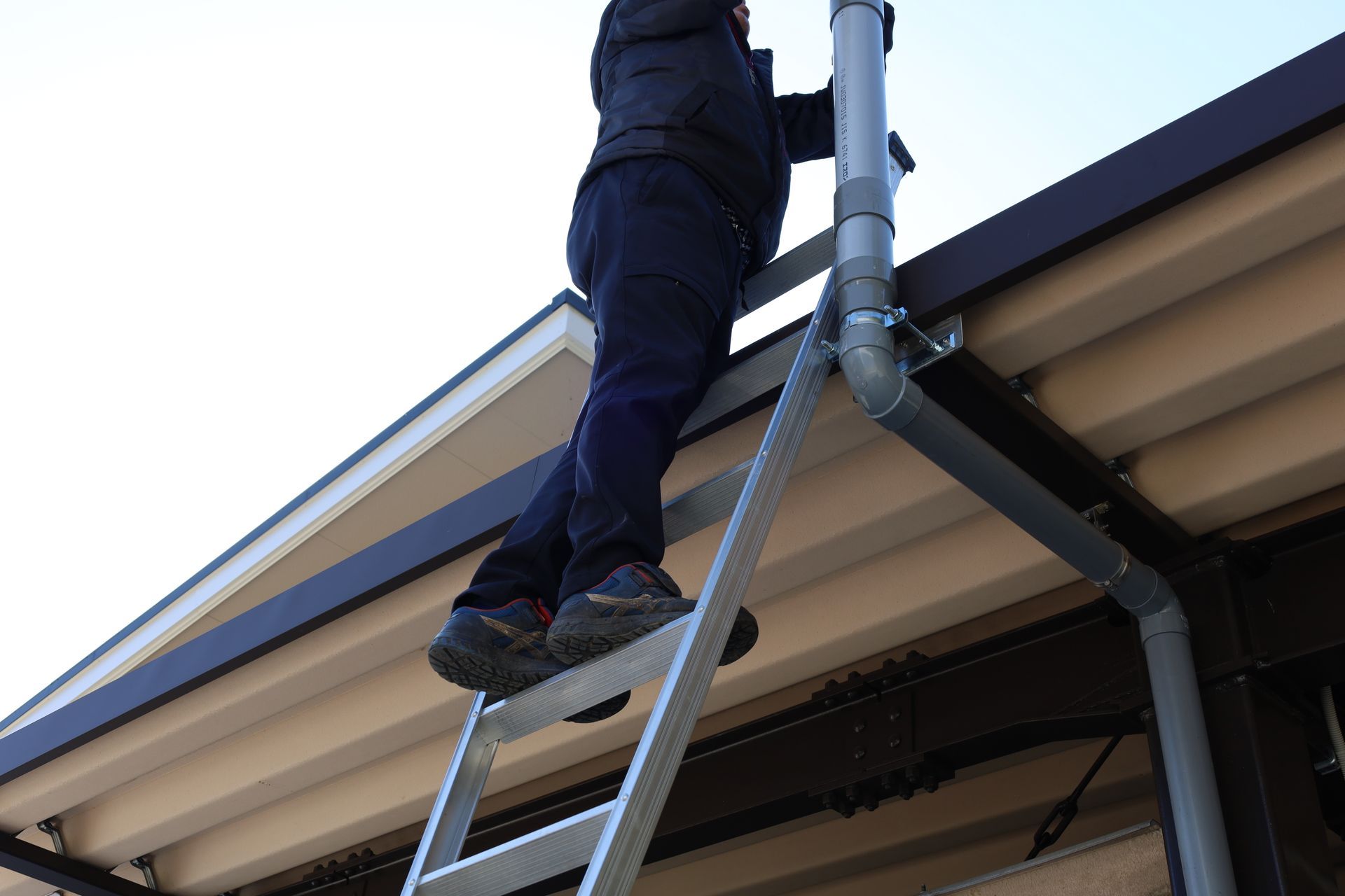 A man on a ladder inspecting a home's roof and gutters.