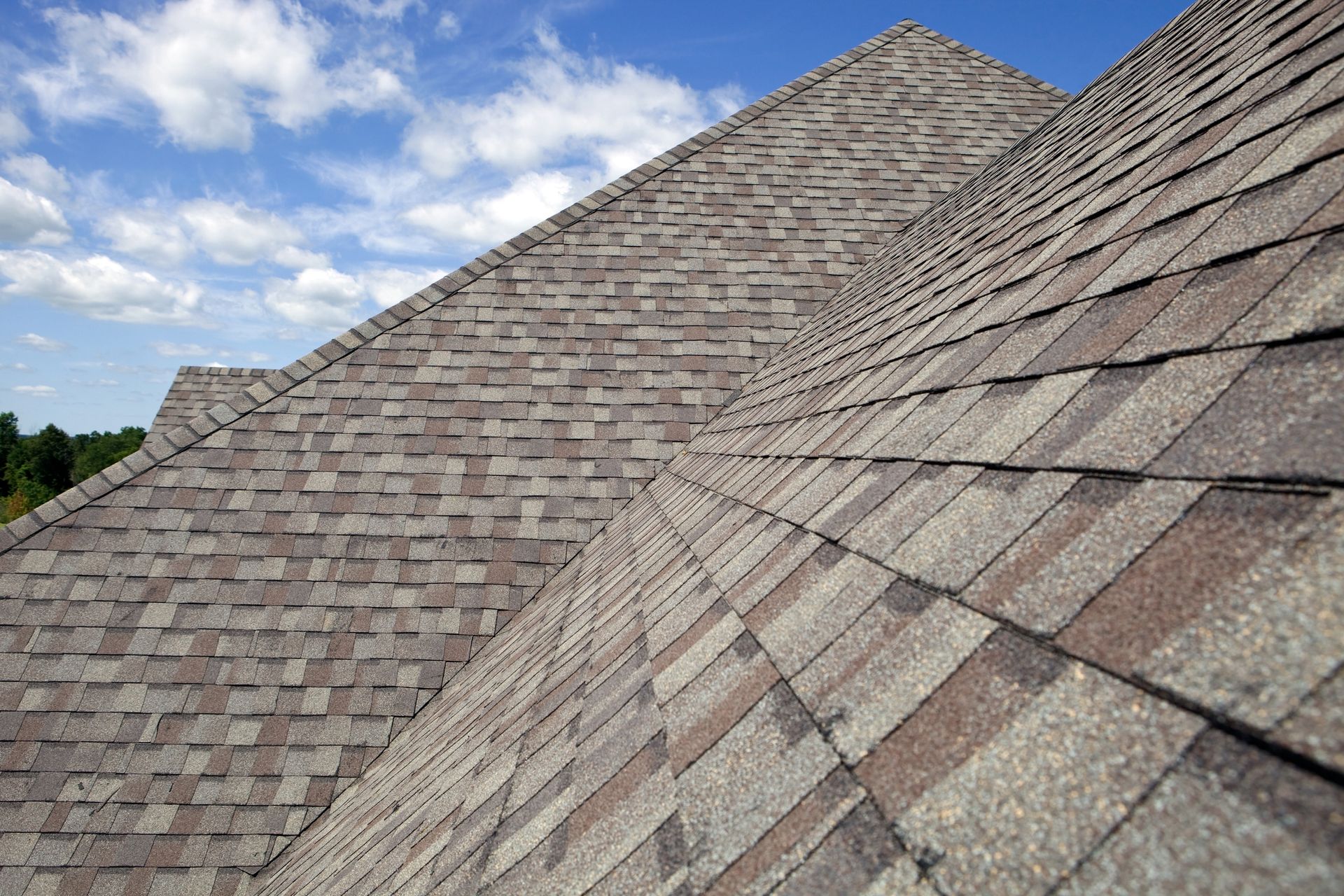 Close-up of a multi-layered shingle roof with shades of brown and gray under a blue sky.