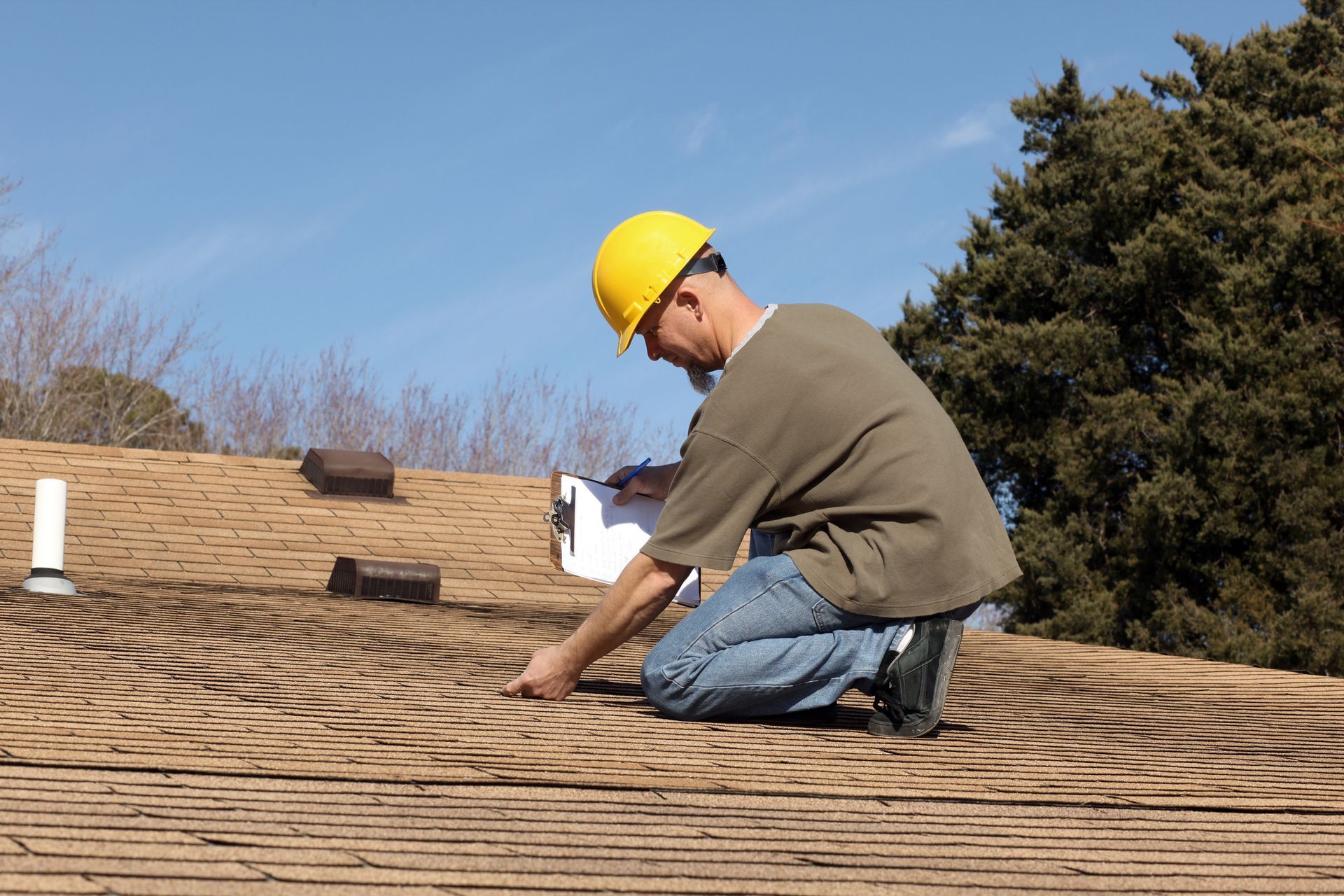 A man wearing a hard hat inspects a roof, performing a thorough home roofing inspection.