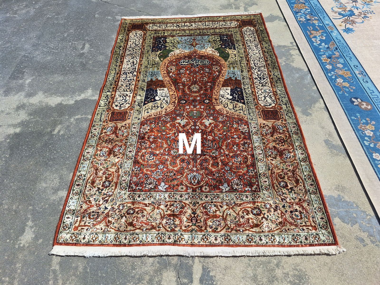 Oriental rug with intricate floral pattern in red, tan, and green; the letter