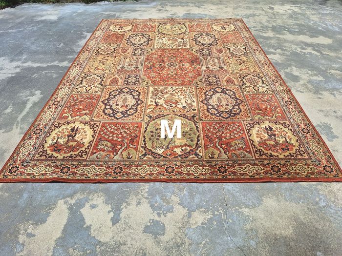 A rectangular rug with an ornate, multi-panel floral pattern in shades of red, cream, and blue, placed on concrete.
