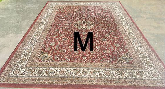 A rug with the letter m on it is sitting on the ground.