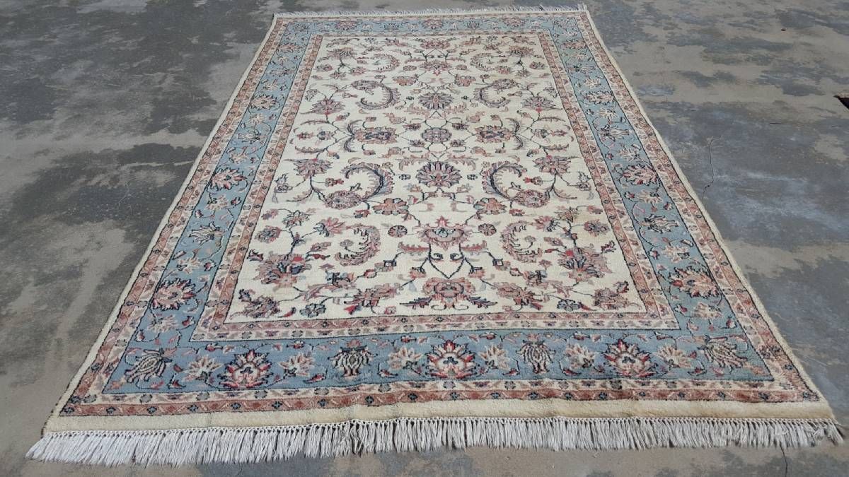 A rectangular area rug with an intricate floral pattern in shades of blue, cream, and red, featuring fringed edges.