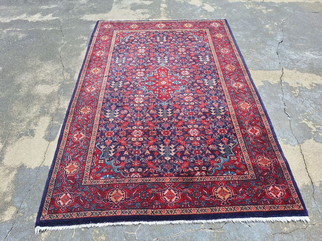 A rectangular rug with a navy blue field, red borders, and intricate, colorful floral and geometric patterns.