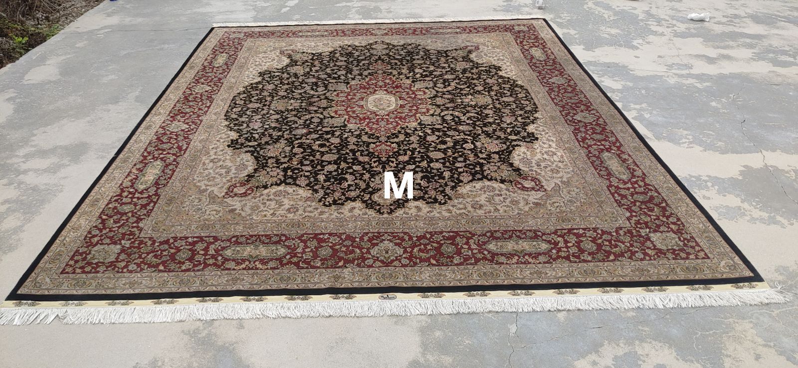A square Persian rug with a cream and burgundy border and center design is displayed outdoors.