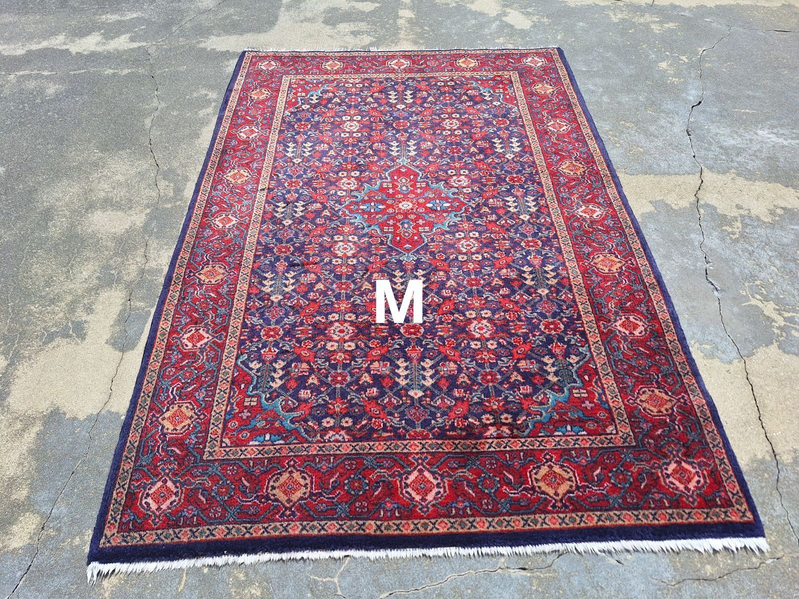 Rectangular Persian rug with a red and blue floral design, lying on a concrete surface.