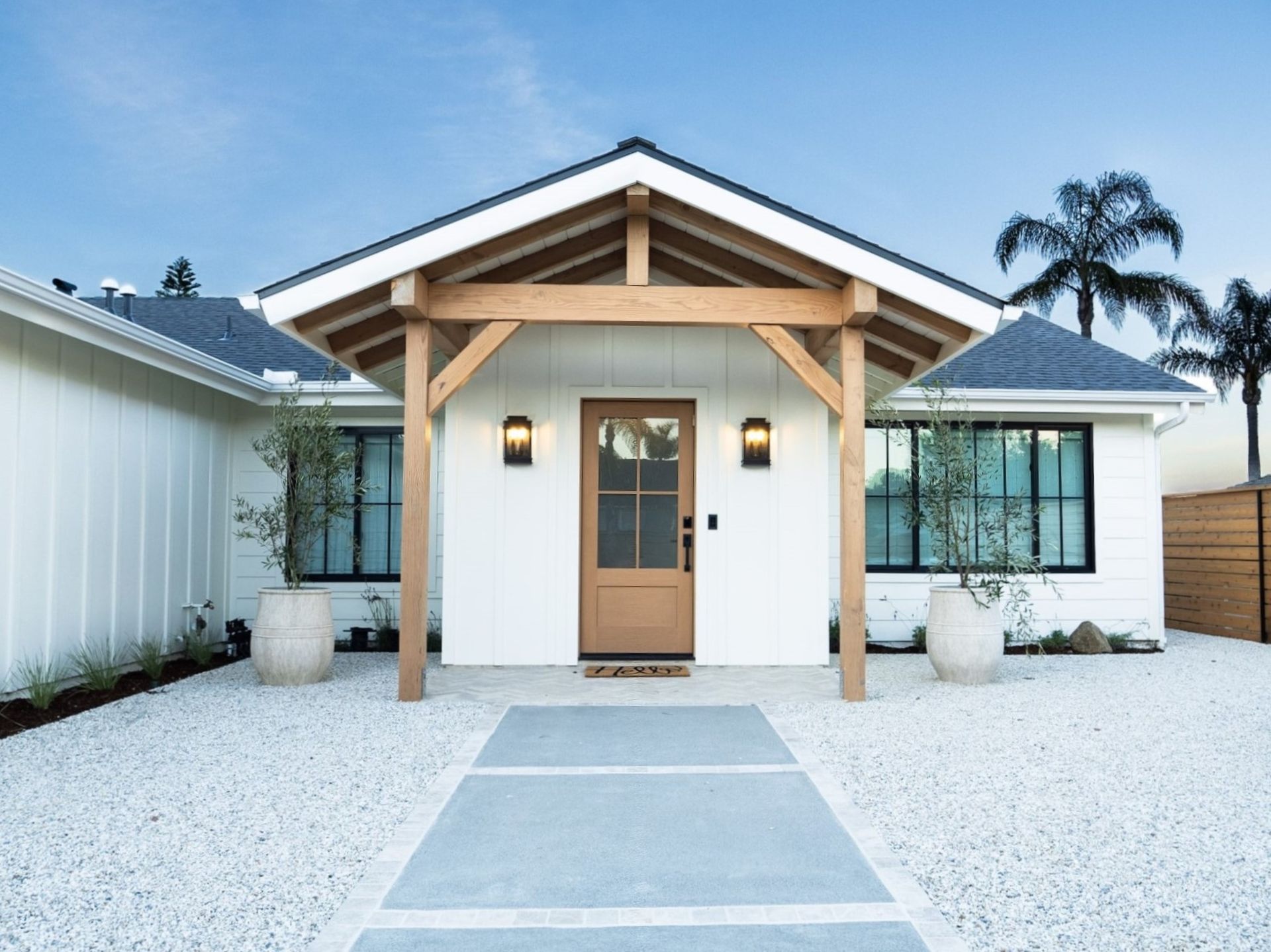 White house with wooden entryway, light fixtures, and concrete pathway.