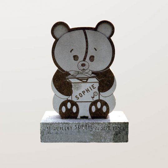 Une pierre tombale sculptée en forme d'ours en peluche, avec le nom « Sophie » et des dates inscrites.