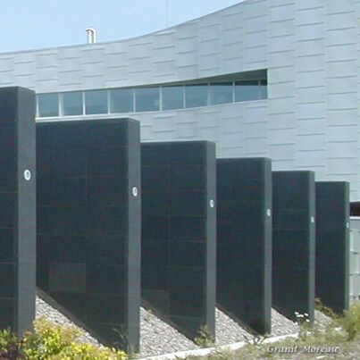 Piliers rectangulaires noirs à l'extérieur d'un bâtiment moderne avec une façade incurvée et de couleur claire.
