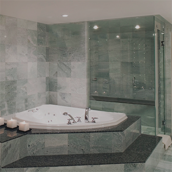 Salle de bain luxueuse avec jacuzzi, carrelage en marbre et douche en verre. Bougies blanches et garnitures gris foncé.