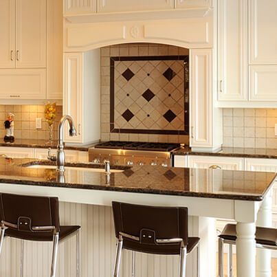 Cuisine couleur crème avec plan de travail en granit foncé et tabourets de bar. La cuisinière est dissimulée sous une crédence en carrelage décoratif.
