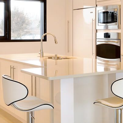 Cuisine blanche moderne avec îlot, tabourets, évier et four et micro-ondes intégrés près d'une fenêtre.