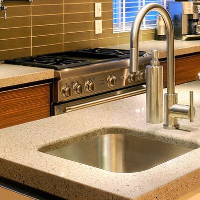 Évier de cuisine avec robinet en acier inoxydable, cuisinière à gaz intégrée et comptoirs de couleur claire.