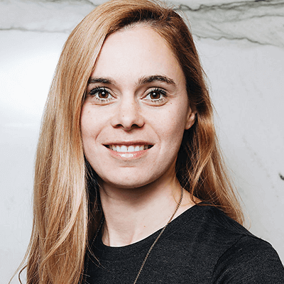 Femme aux cheveux blonds, souriante, vêtue d'une chemise noire, devant un fond en marbre.