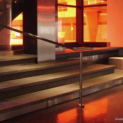 Escalier avec rampe métallique, baigné de lumière orange. Des marches en béton mènent à l'étage ; fenêtre en arrière-plan.