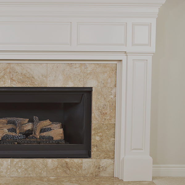 Cheminée avec manteau blanc, contour en carrelage beige et foyer noir avec fausses bûches.