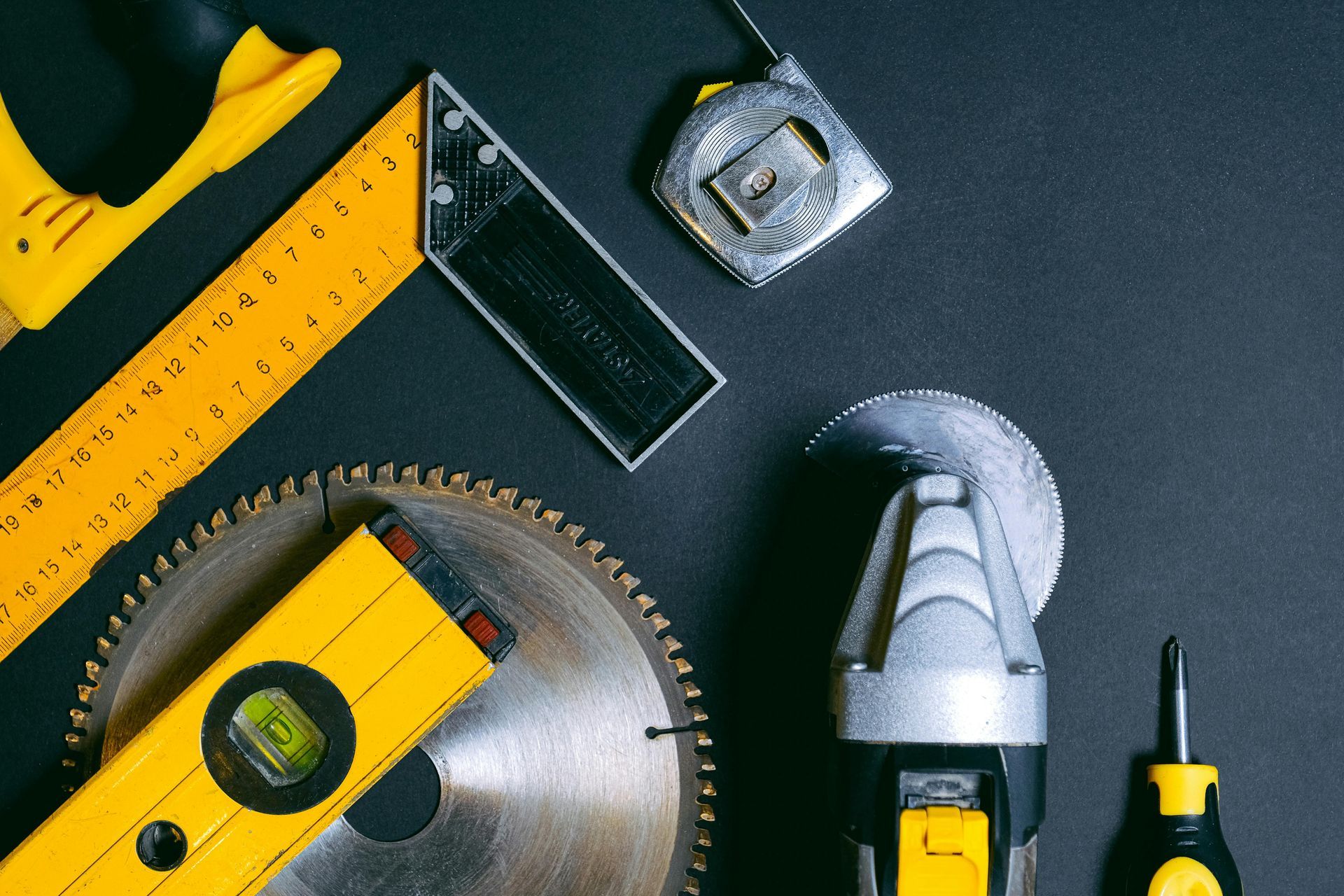 Yellow and silver construction tools arranged on a black surface.