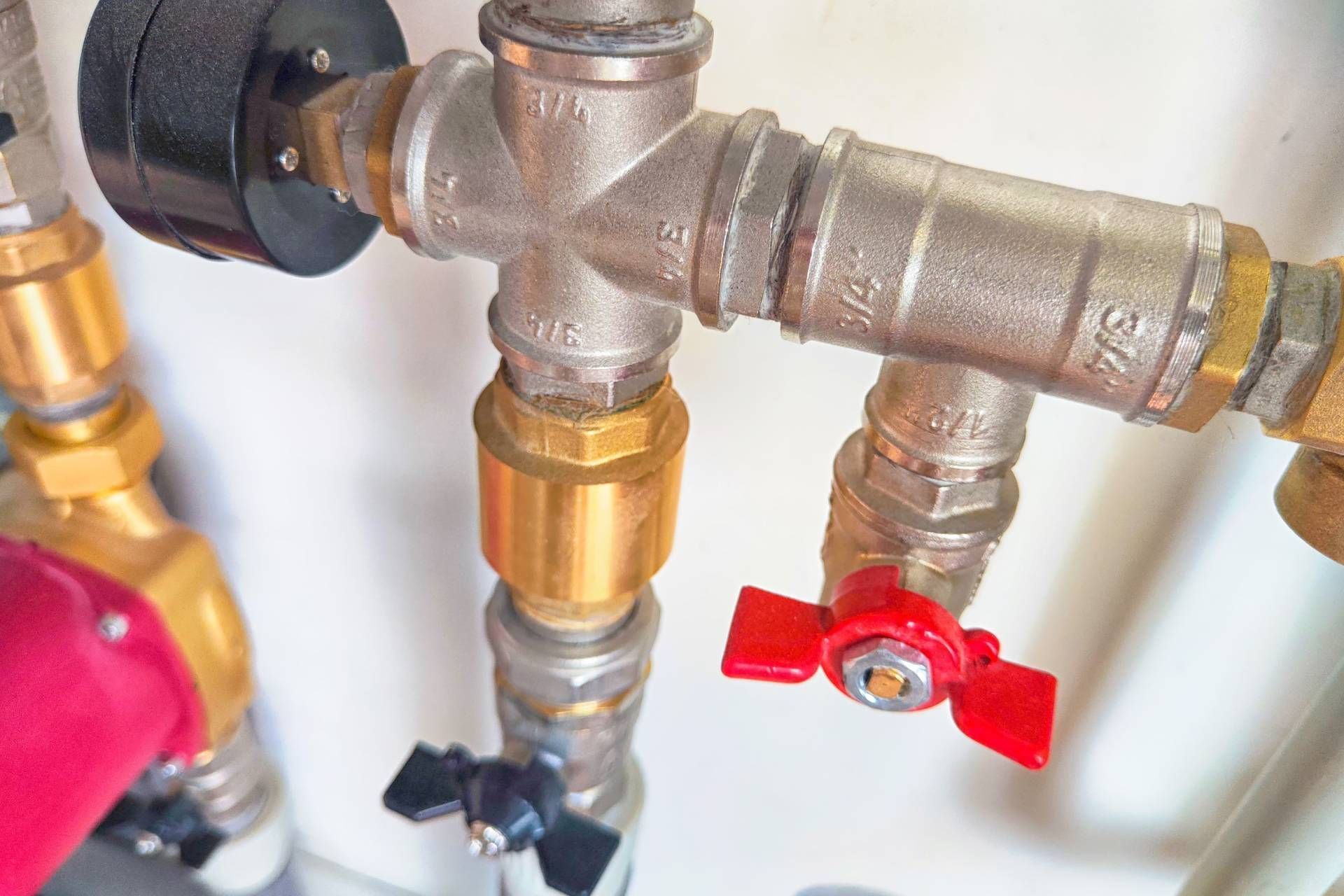 Close-up of plumbing pipes and valves, including a red handle valve and a black pressure gauge.