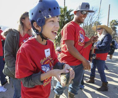 A young boy wearing a blue helmet is holding a fish.