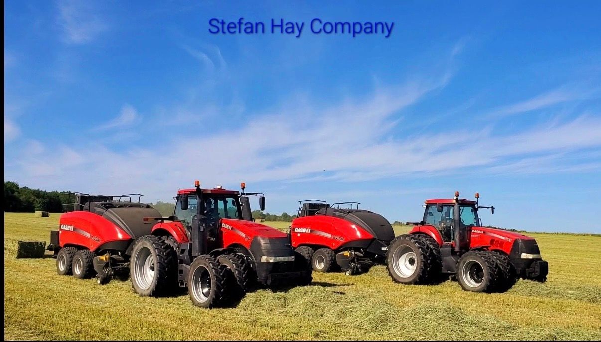 Two red tractors pulling hay balers in a field under a blue sky. "Stefan Hay Company" text above.