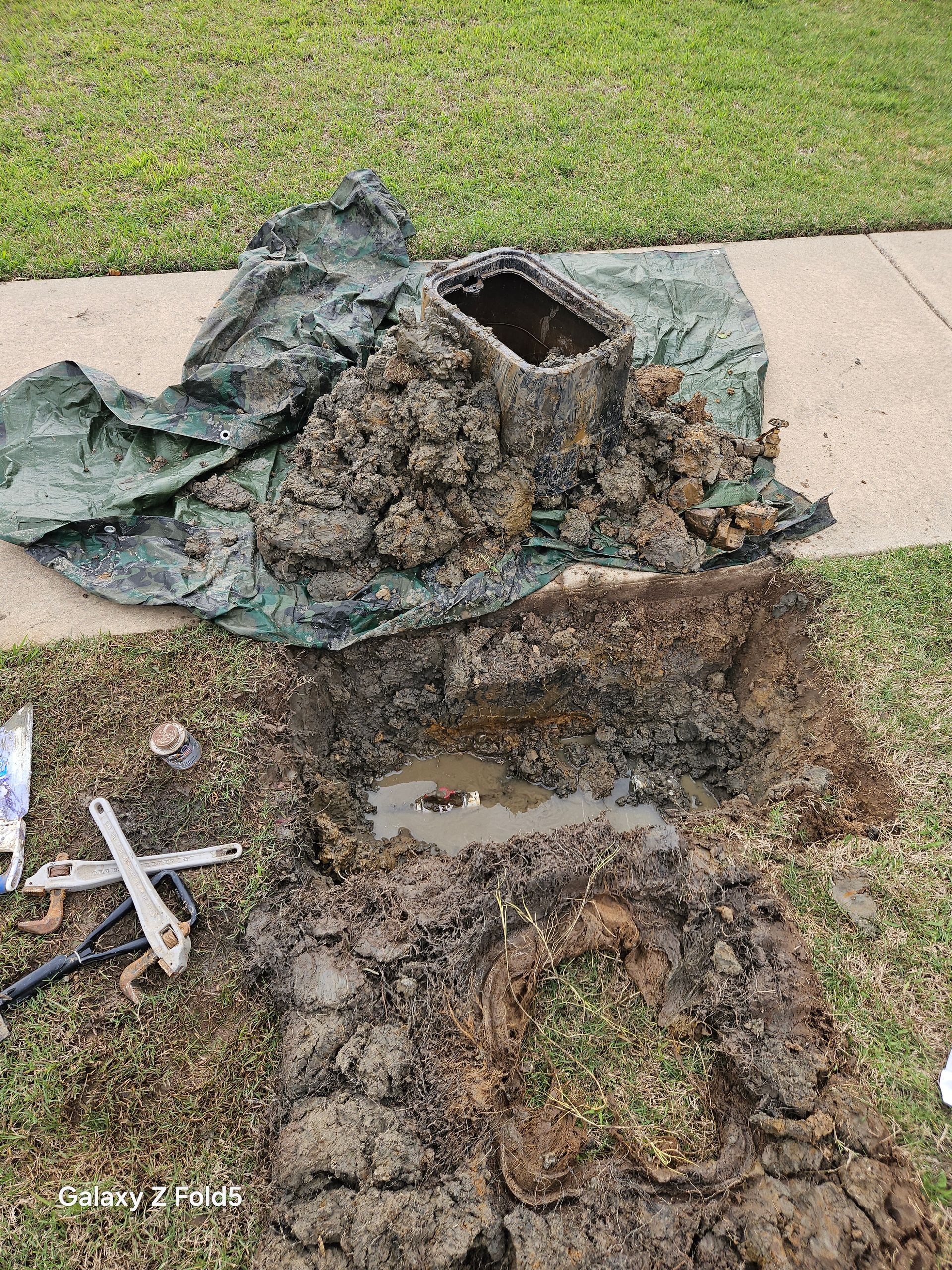 A pile of dirt is sitting on top of a grassy field next to a sidewalk.