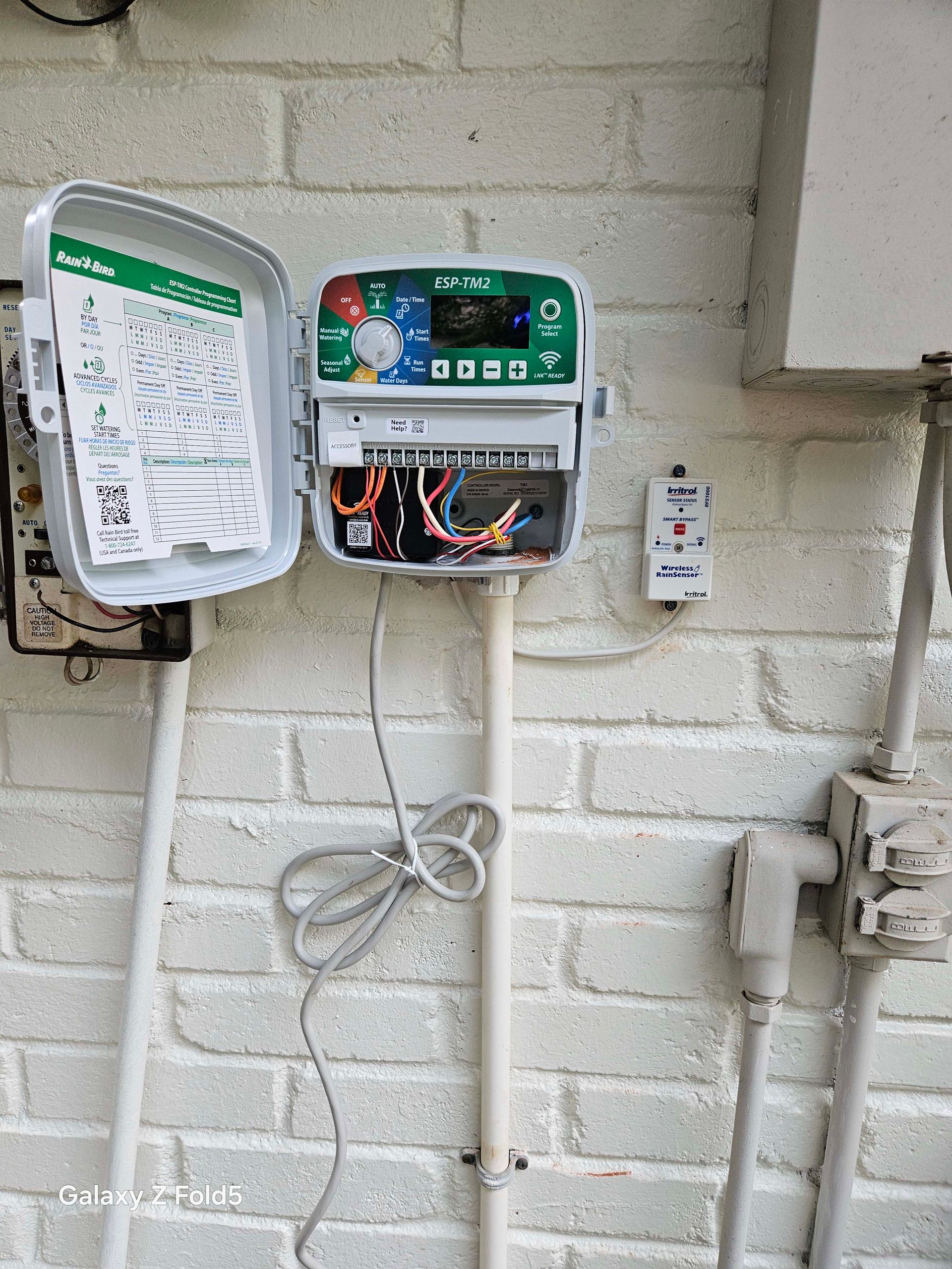 A sprinkler controller is sitting on a white brick wall.