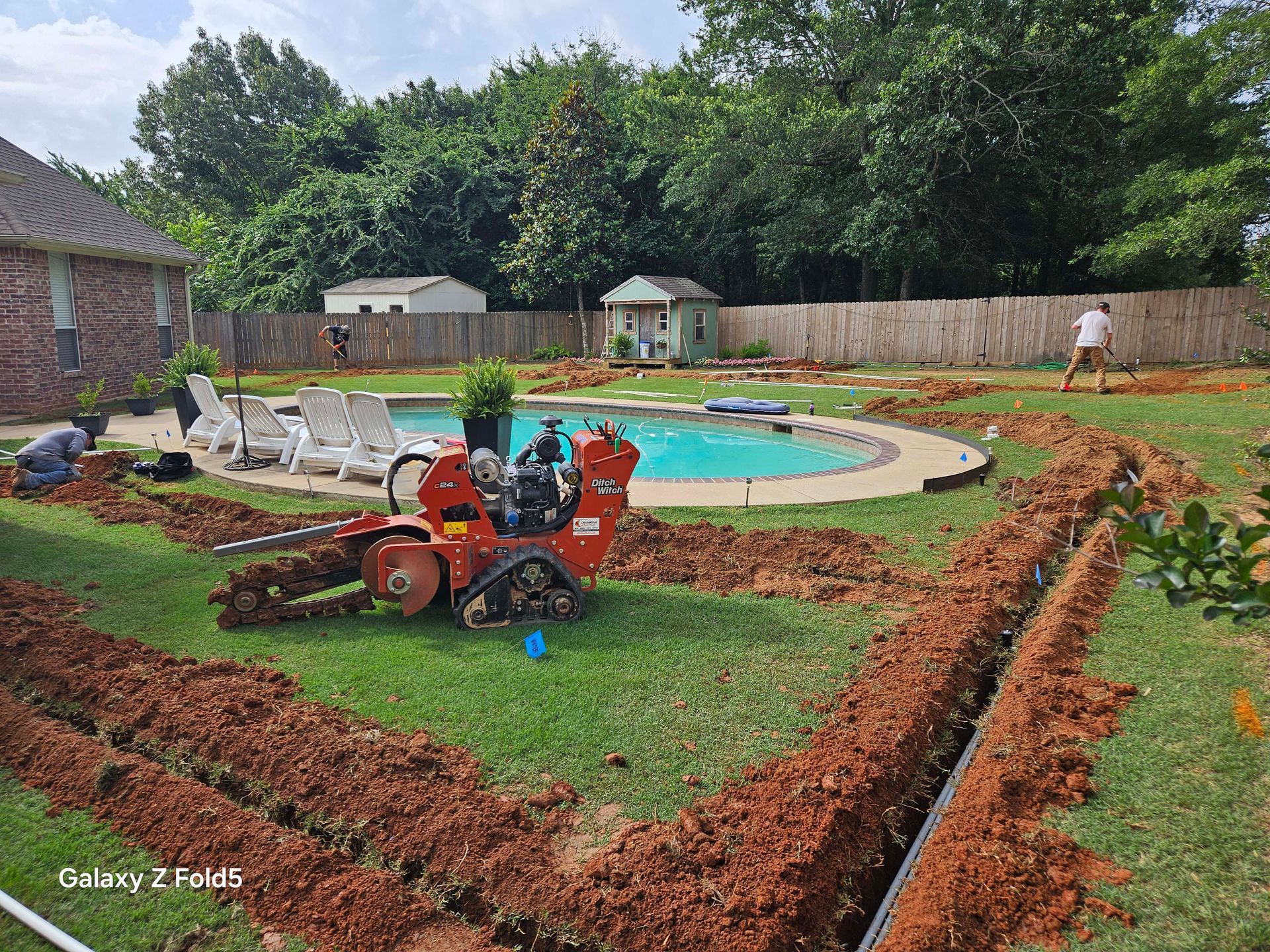 A tractor is digging a trench in a backyard next to a pool.