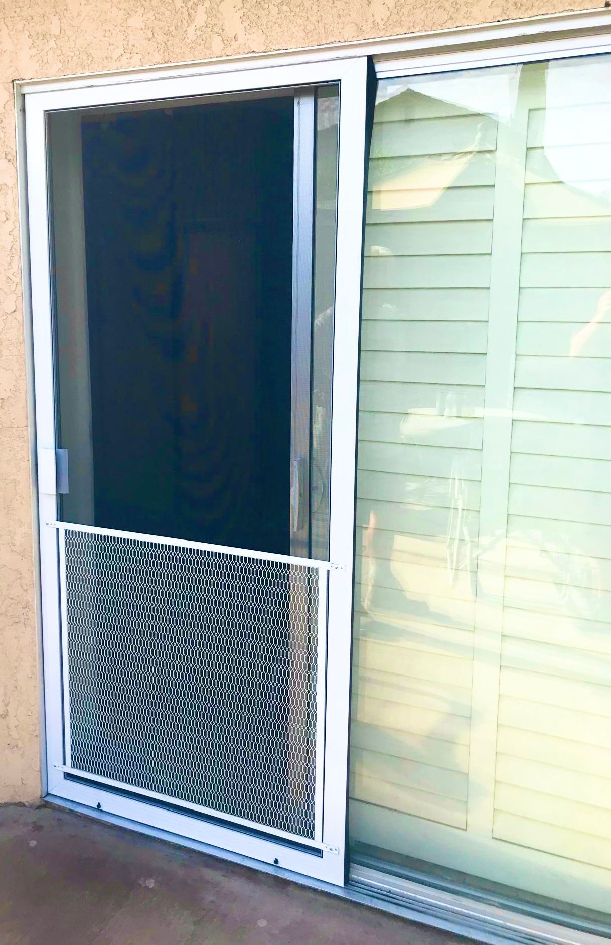 A white sliding screen door with a decorative metal pet grille at the bottom, installed on a sliding glass door track.