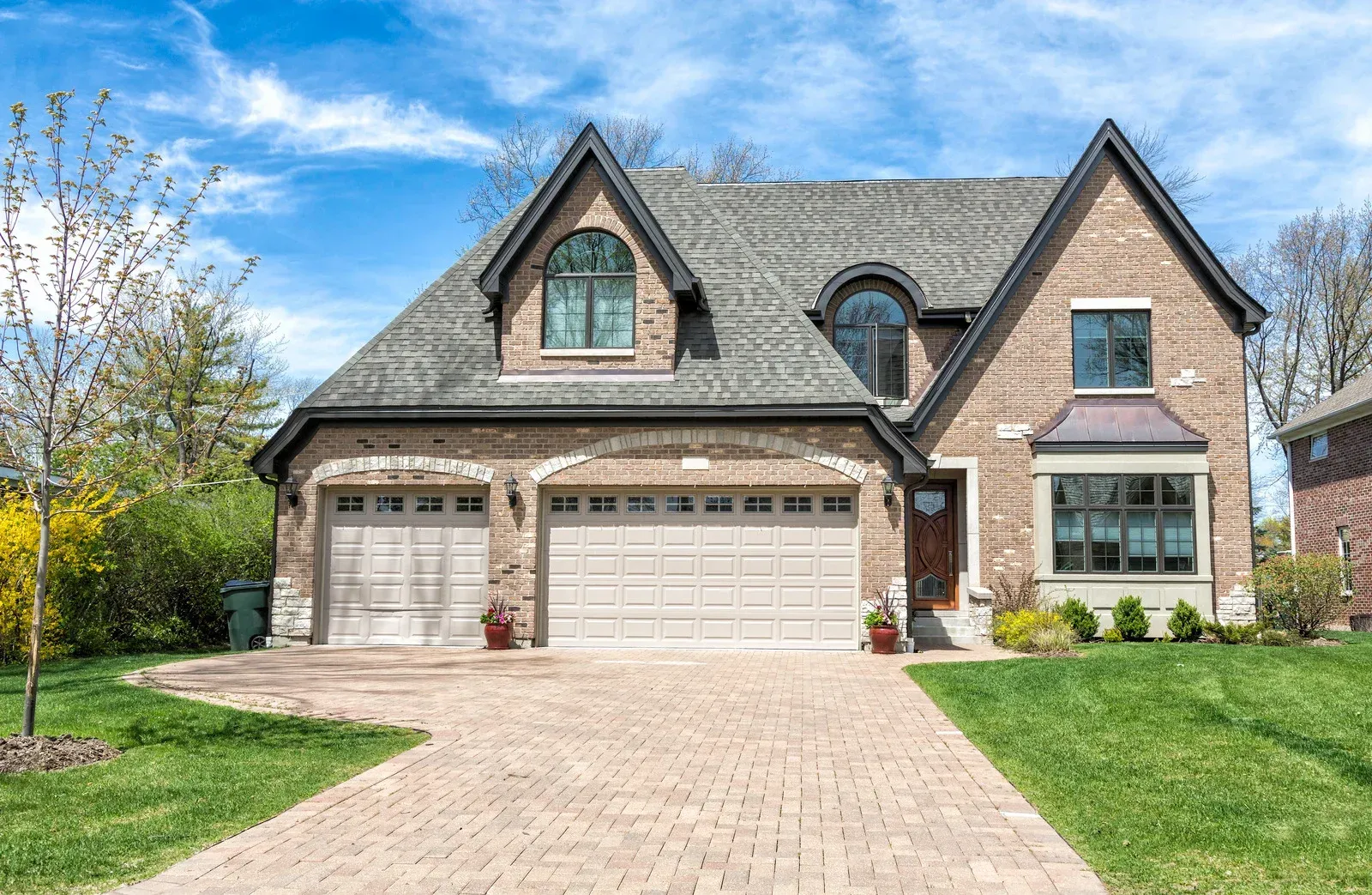 Brick suburban house with three-car garage, stone facade, and paved driveway under a blue sky
