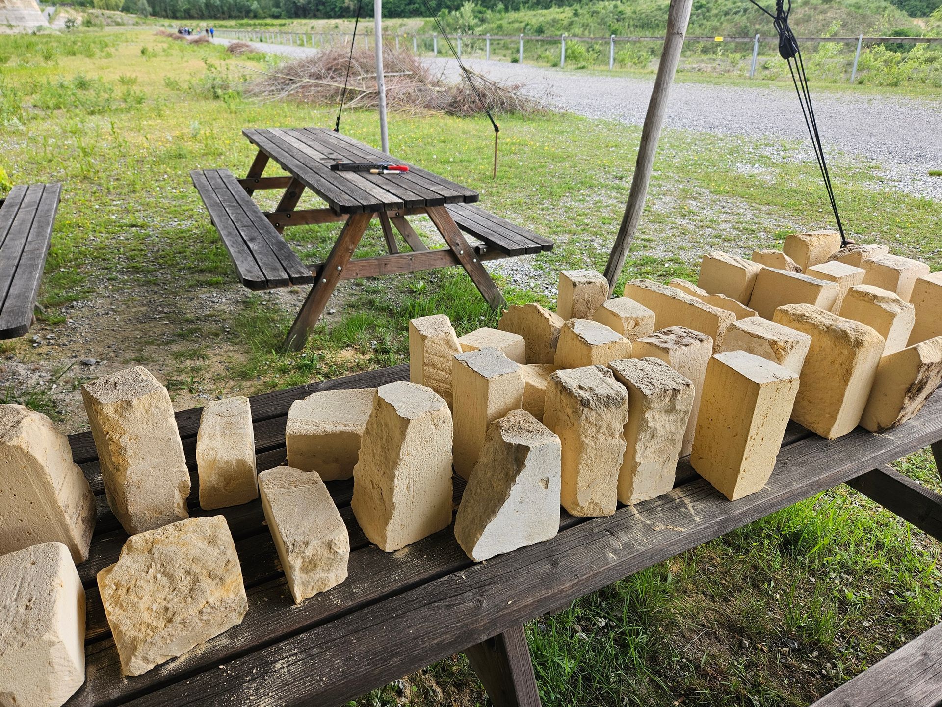 Rijen gehouwen stenen blokken liggen  op een houten bank buiten, vlakbij een picknicktafel.