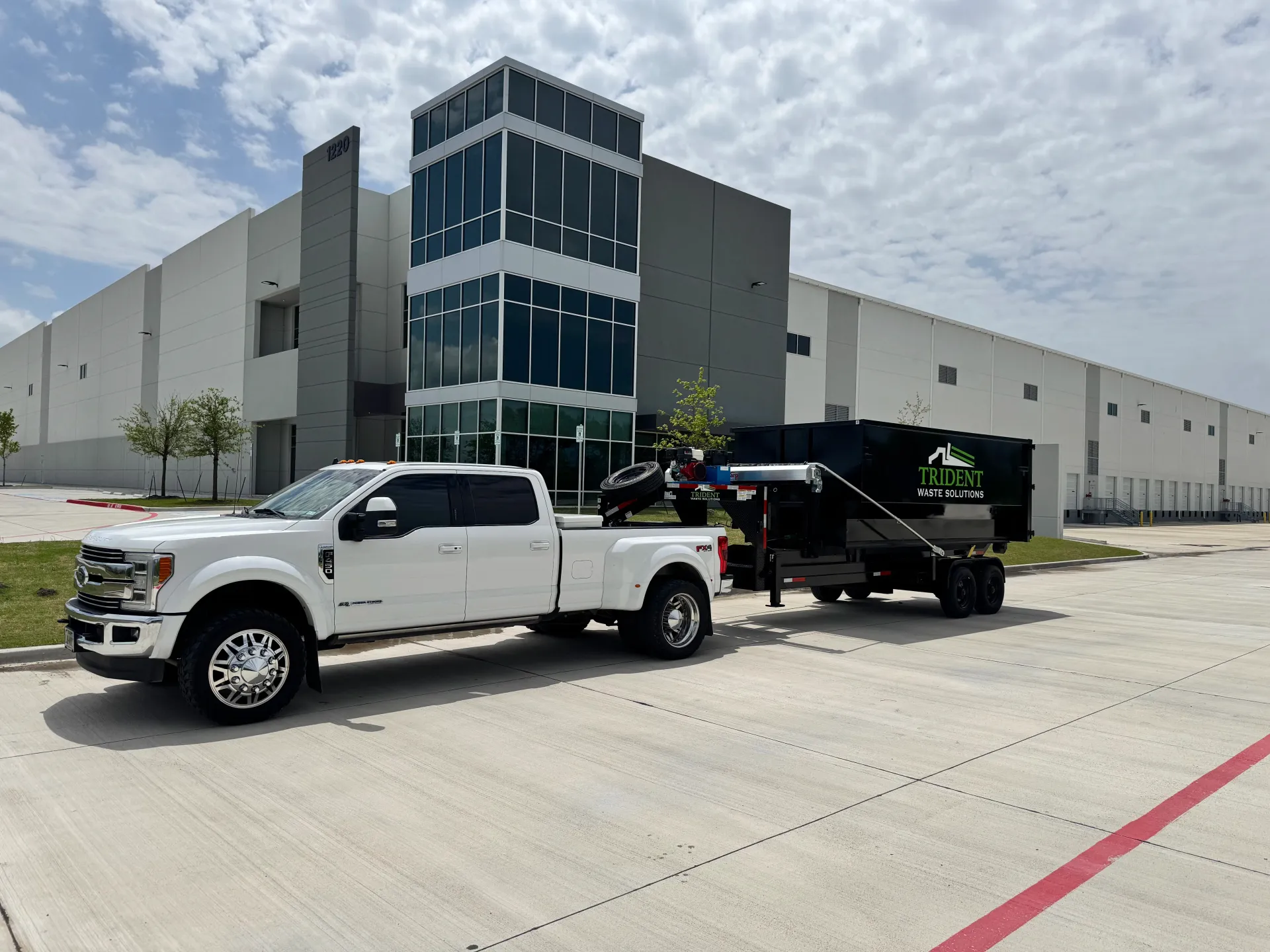 A white truck is towing a trailer in front of a large building.