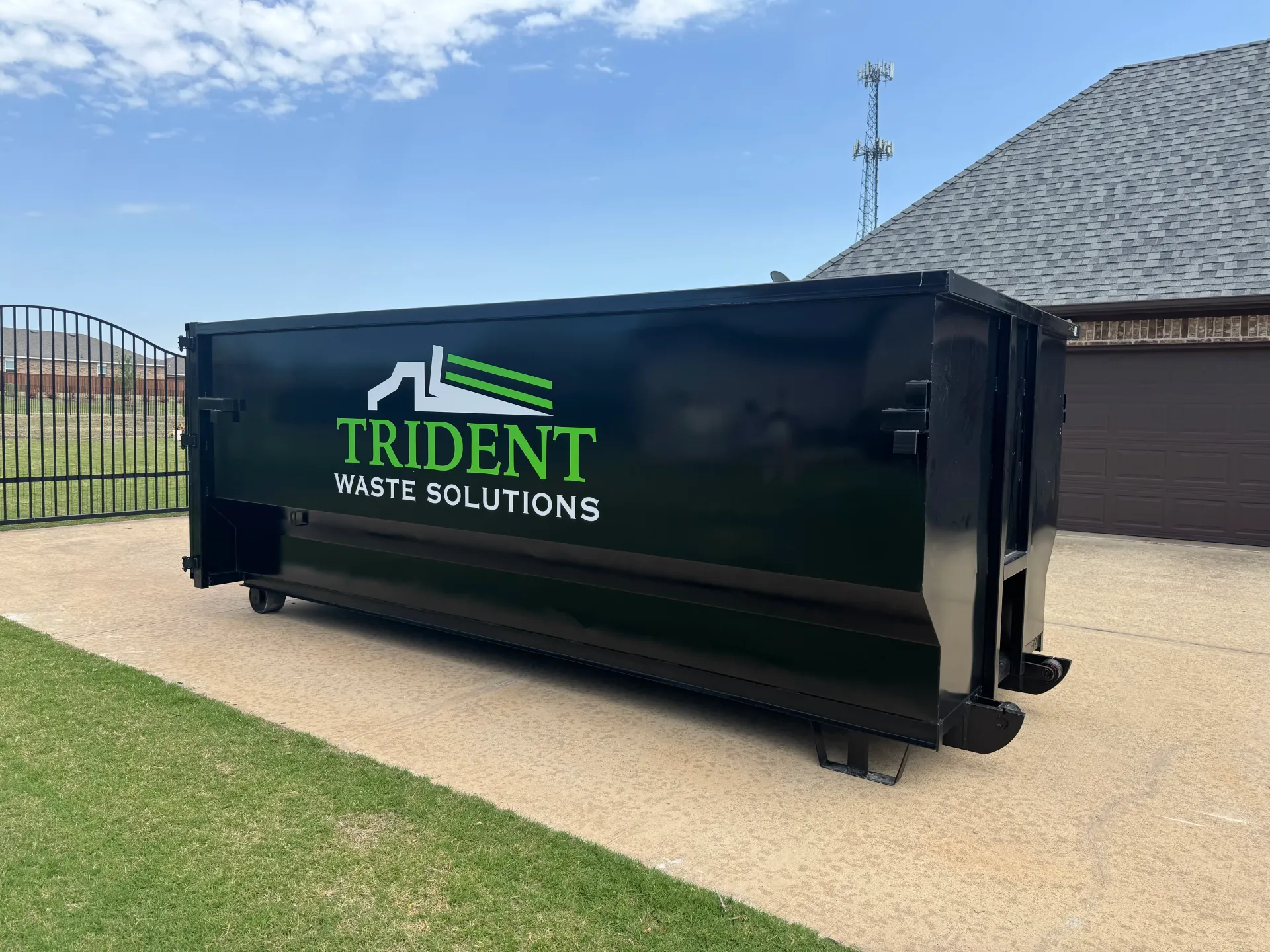 A green dumpster is parked in front of a house.