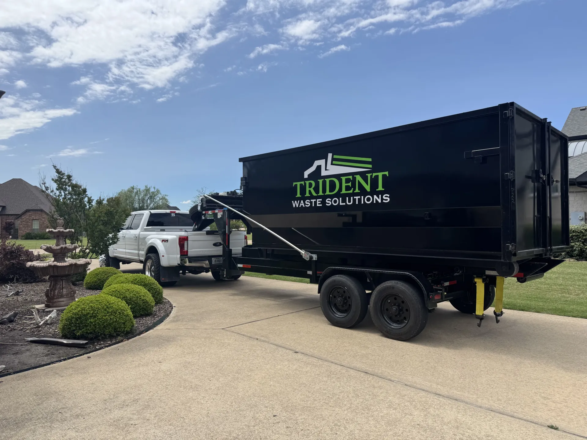 A green dumpster is parked in front of a brick building.